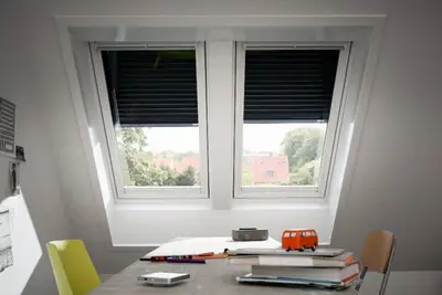 Twee wit afgewerkte dakramen met gedeeltelijk gesloten rolluiken boven een bureau